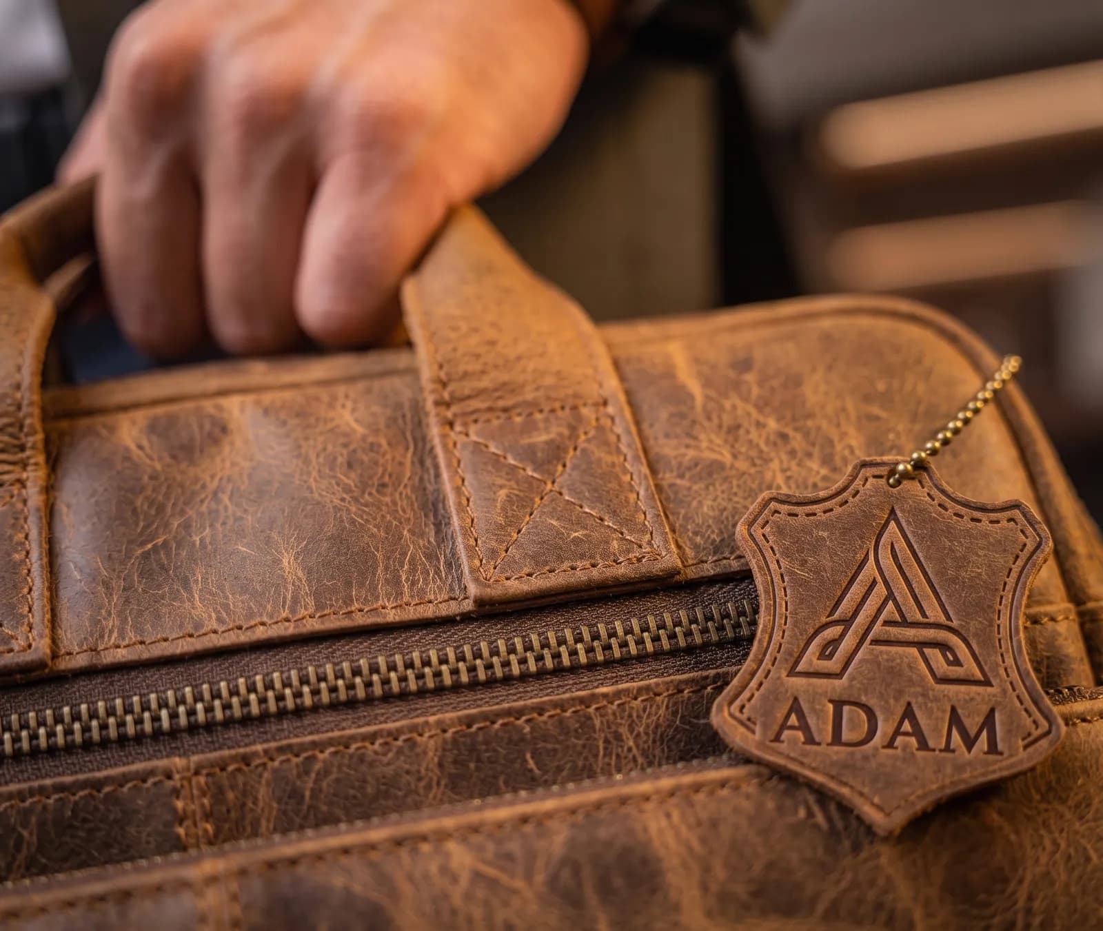Close-up of the leather handle, brass zipper, and Adam logo tag on the Art 301 laptop bag